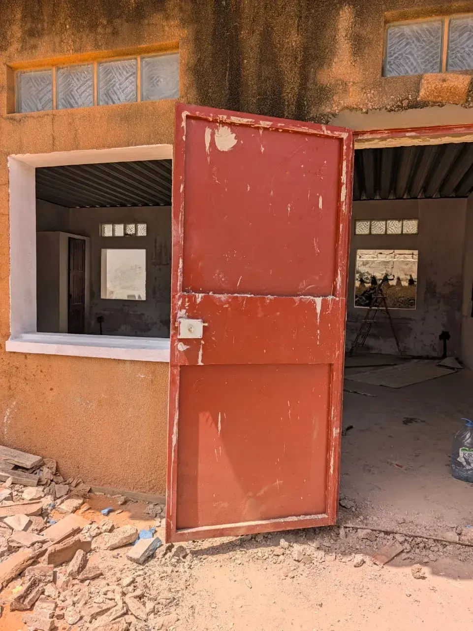 Une porte métallique rouge ouverte sur un local en cours de rénovation.