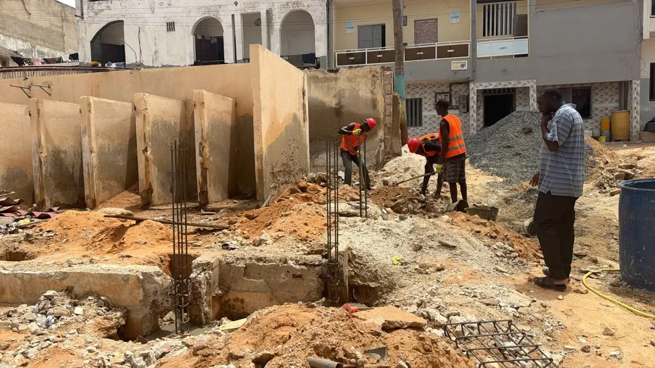 Trois ouvriers en gilet orange travaillent aux fondations sous le regard d’un chef de chantier.