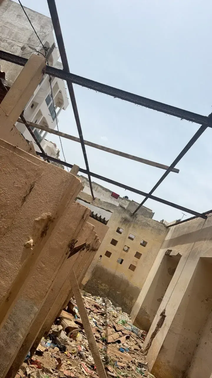 Vue en contre-plongée d’une charpente métallique posée au-dessus de murs anciens.